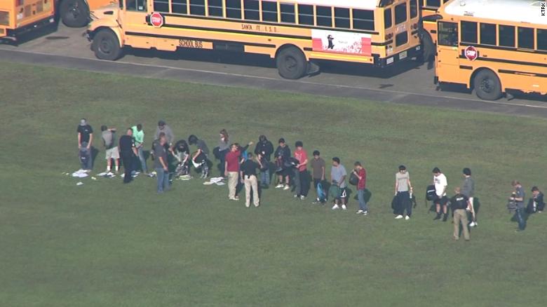 Students empty their backpacks for officers outside the school.