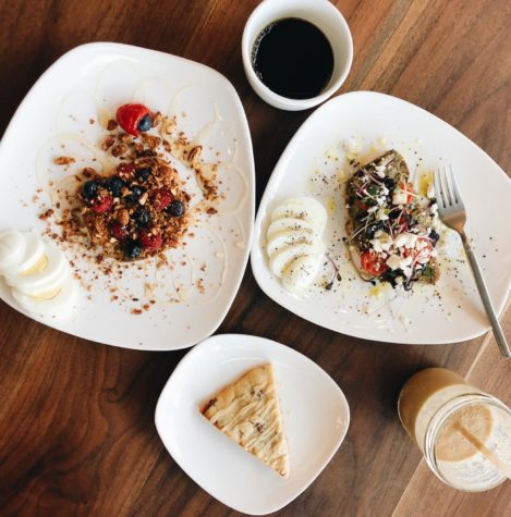 Breakfast at Daily Clean Food and Drink featuring a Gluten Free Scone, Energizer Monkey Smoothie, a glass of regular drip coffee, Holy Guacamole toast, and Loaded PB and J toast on Gluten Free bread.