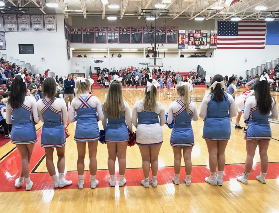 Varsity cheerleaders stand on the sideline