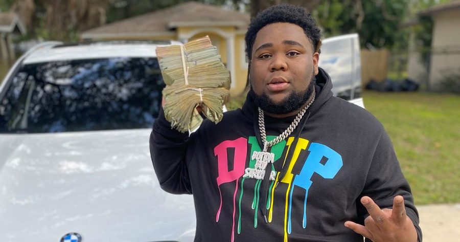 Rapper Rod Wave showing off a stack of U.S currency while showing off his diamond chain.