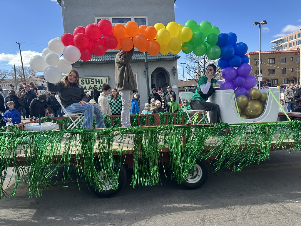 A rainbow balloon arch is paraded down Phillips Avenue on a grass-decorated float. 