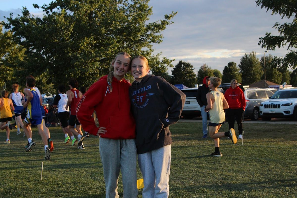 As the boys junior varsity race takes place behind them, JV athletes Ryan Tibbetts and Melanie Herman smile for a photo.