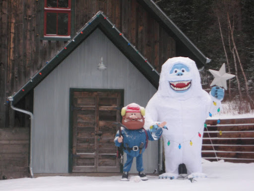 Two characters from “Rudolph the Red-Nosed Reindeer” are placed in front of a cabin to welcome visitors.
